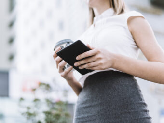 low-angle-view-businesswoman-holding-smartphone-disposable-coffee-cup-outdoors